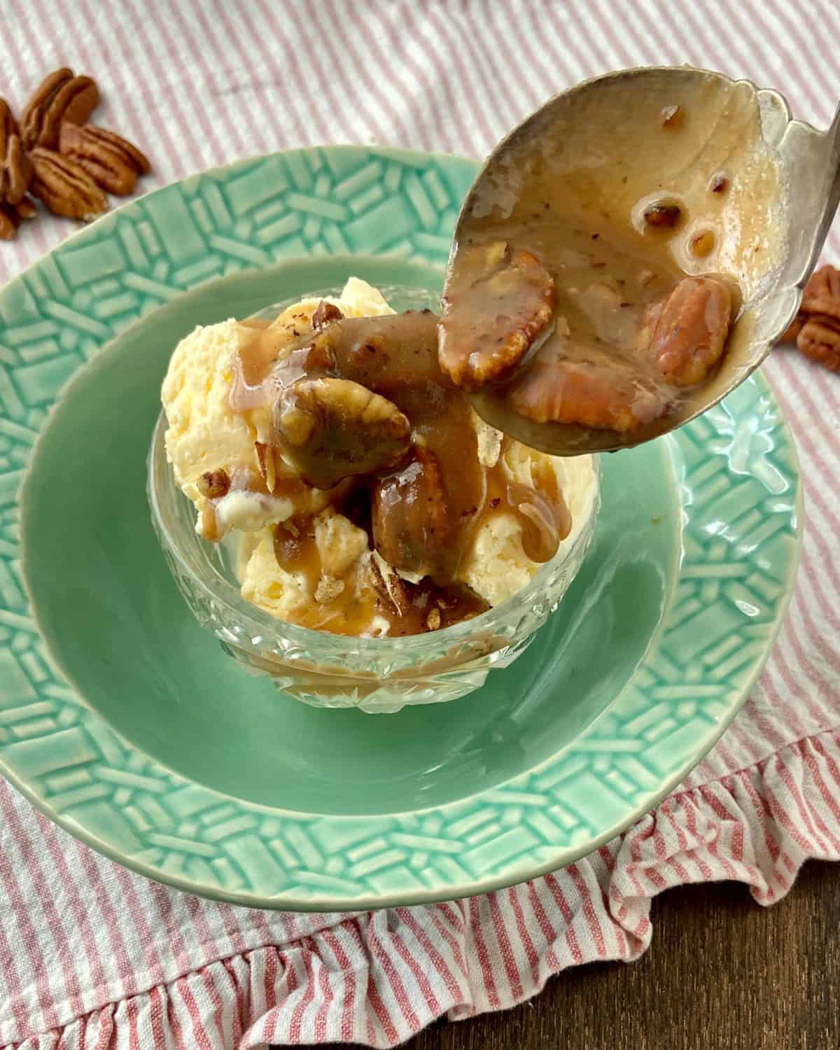 Toasted pecan praline sauce in spoon being drizzled over vanilla ice cream.
