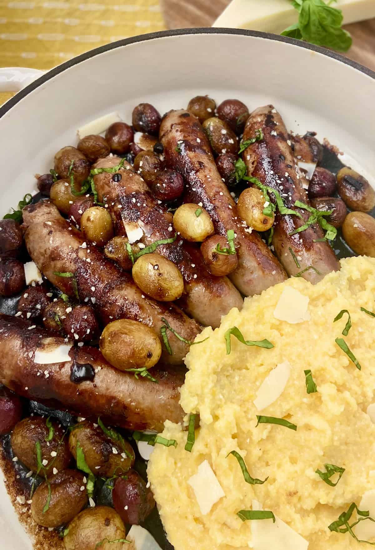 Italian Sausage and grapes with a side of polenta in white skillet.
