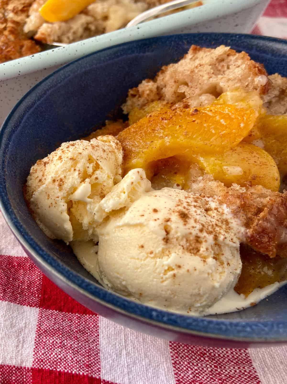 Peach cobbler with vanilla ice cream in blue bowl.