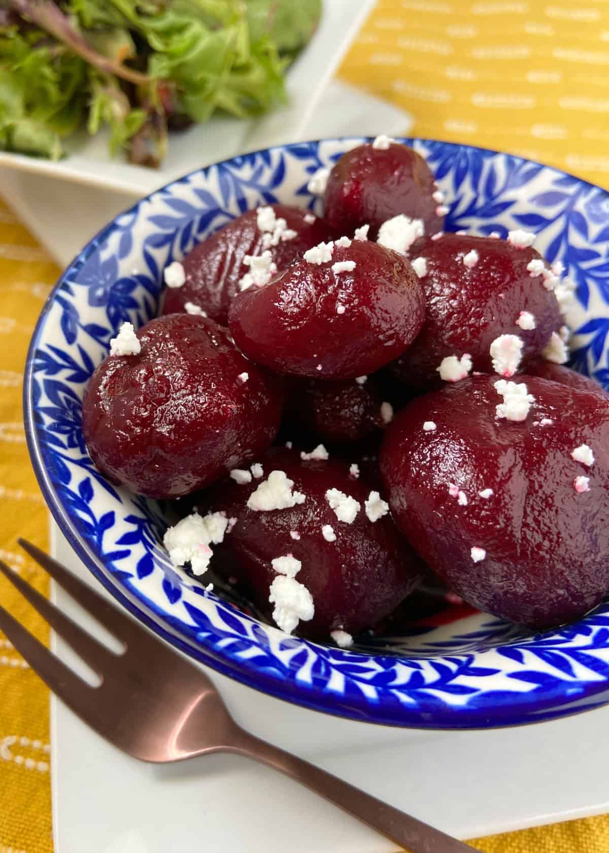 Whole pickled beets in decorative blue bowl garnished with crumbles of goat cheese.