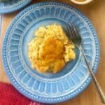 Scoop of corn pudding on blue plate with fork.