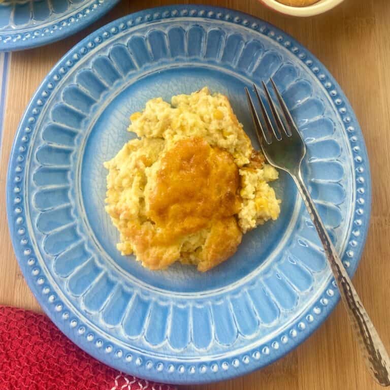 Scoop of corn pudding on blue plate with fork.