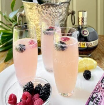 Chambord champagne cocktail in stemless champagne flute on white serving platter.