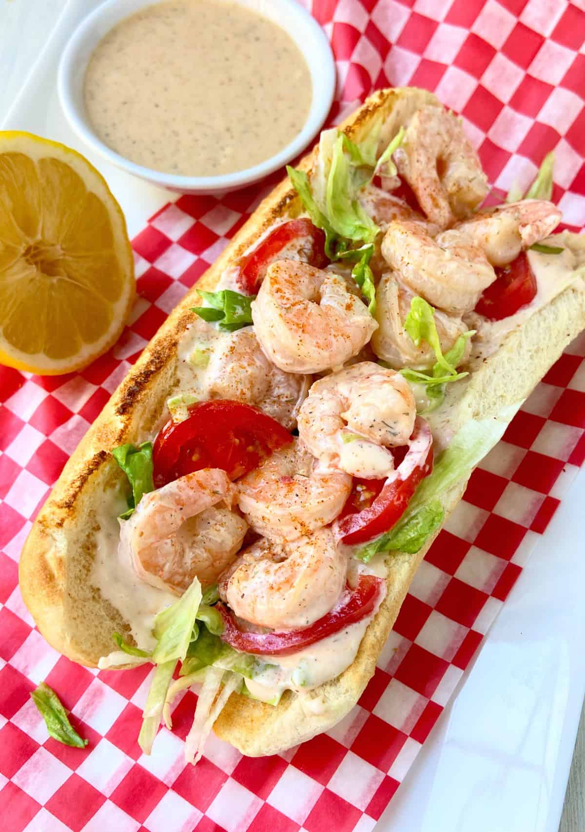 Shrimp Po' Boy sandwich open-faced on a red and white checkered plate.