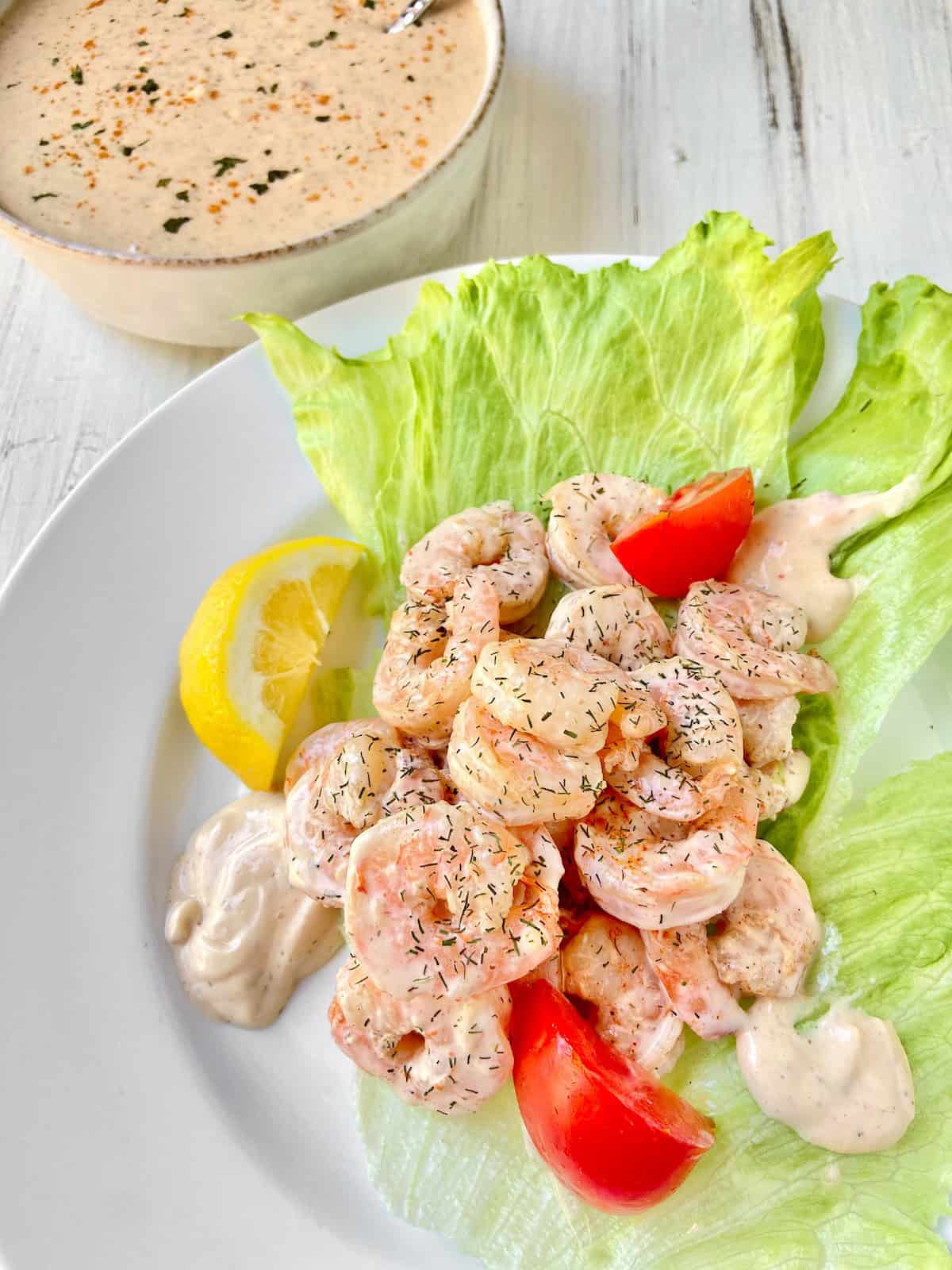 Shrimp Remolaude Salad on white plate with tomato wedges and a lemon.