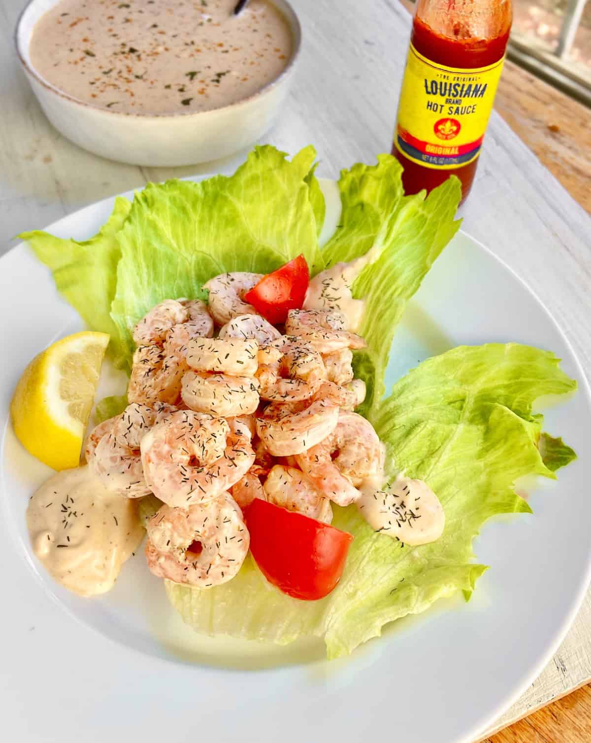Shrimp remolaude salad with tomato wedges on white plate.