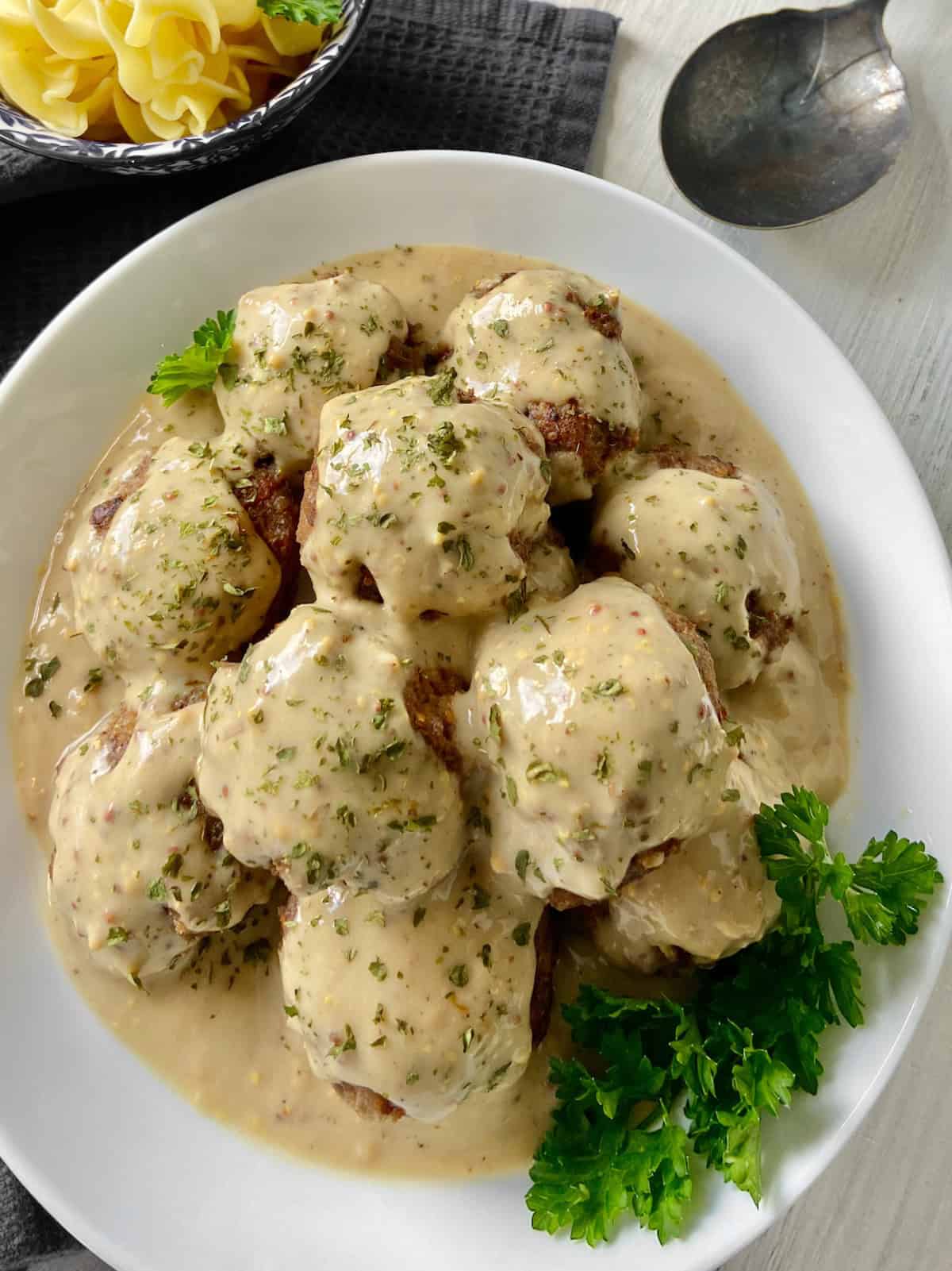 Swedish meatballs in gravy in white serving bowl garnished with parsley.