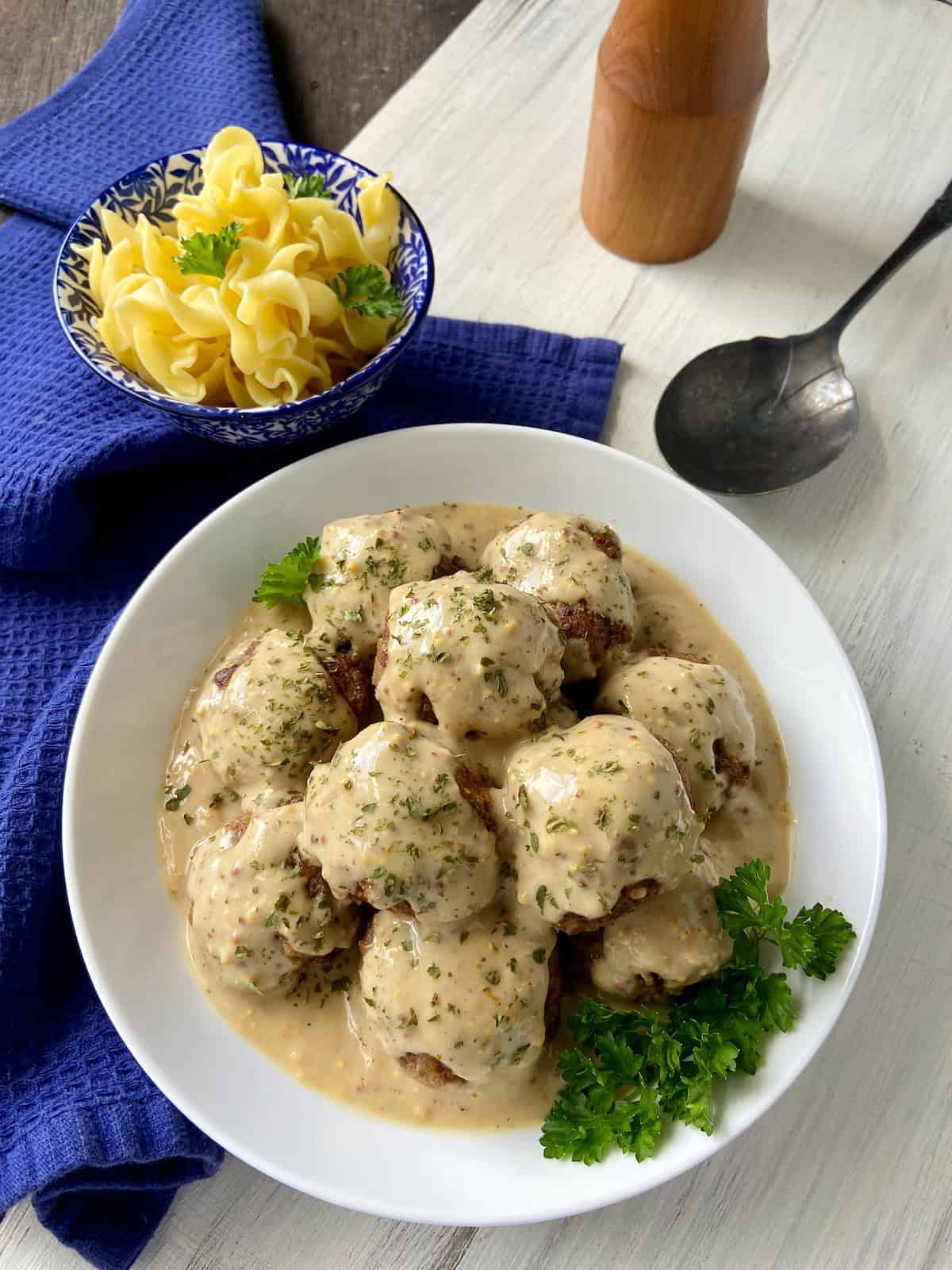 Swedish meatballs and gravy in white serving bowl garnished with fresh parsley.