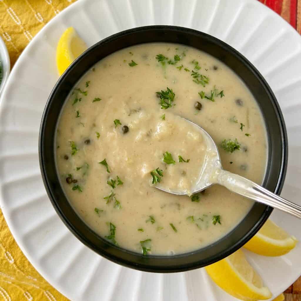 White bean soup on spoon in black bowl.