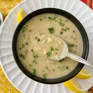 White bean soup on spoon in black bowl.