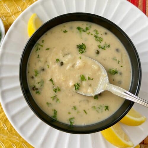 White bean soup on spoon in black bowl.