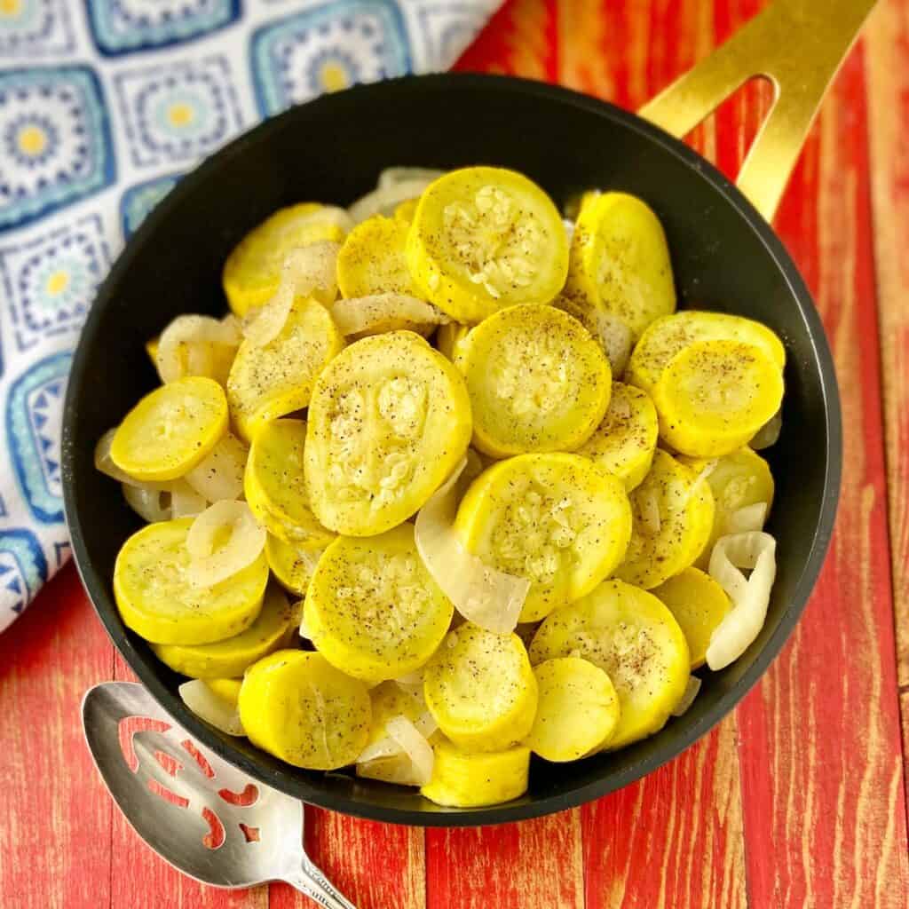 Sauteed yellow squash and onions in black skillet.