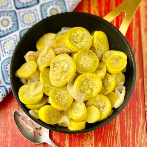 Sauteed yellow squash and onions in black skillet.
