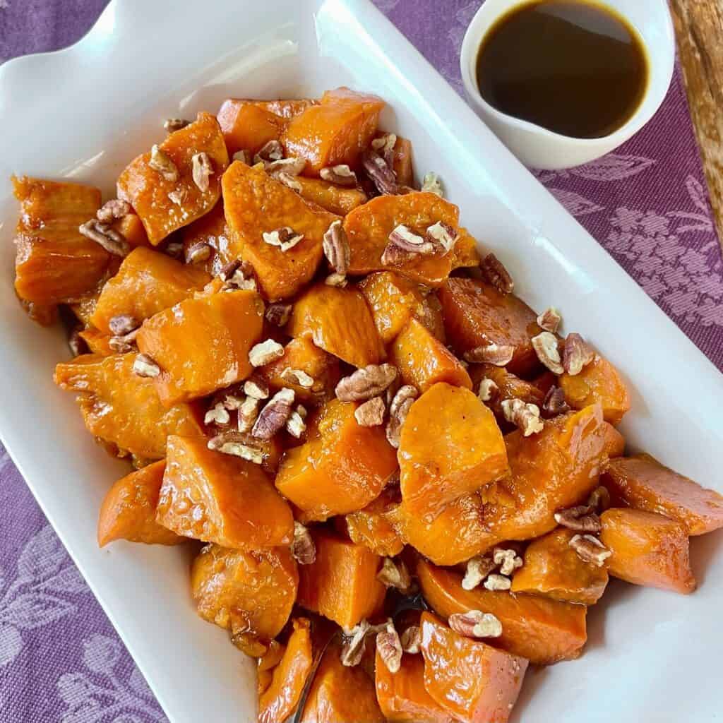 Candied sweet potatoes with chopped pecans on white platter.