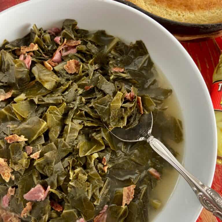 Collard greens with ham in white bowl with serving spoon.