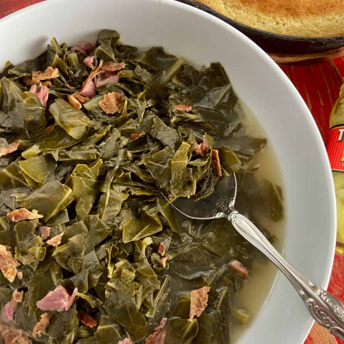 Collard greens with ham in white bowl with serving spoon.