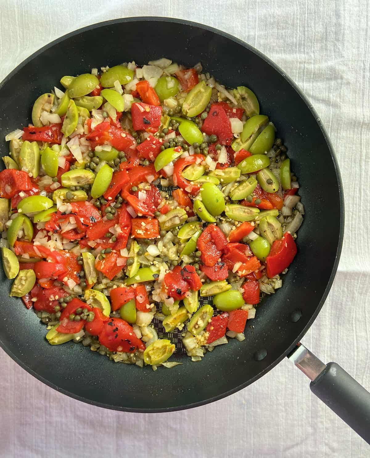 Sauteed roasted red peppers, olives, garlic and capers in saucepan.