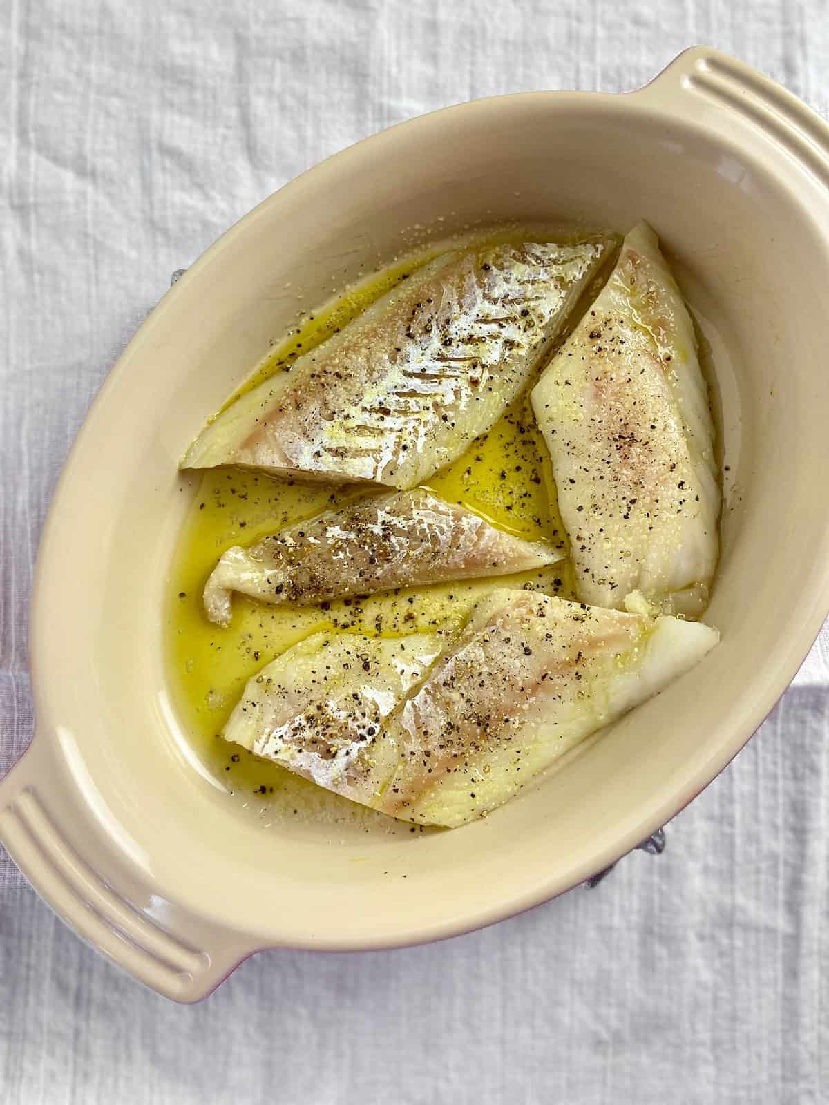 Cod fillets in olive oil in oval baking dish.