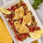 Sicilian baked cod with garlic breading resting on a bed of roasted red peppers and olives.