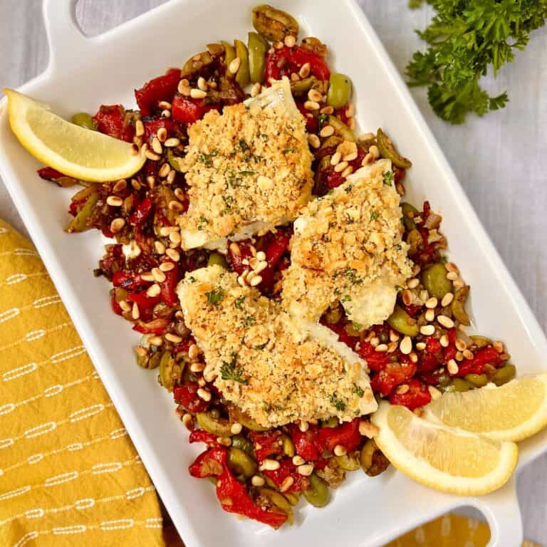 Sicilian baked cod with garlic breading resting on a bed of roasted red peppers and olives.