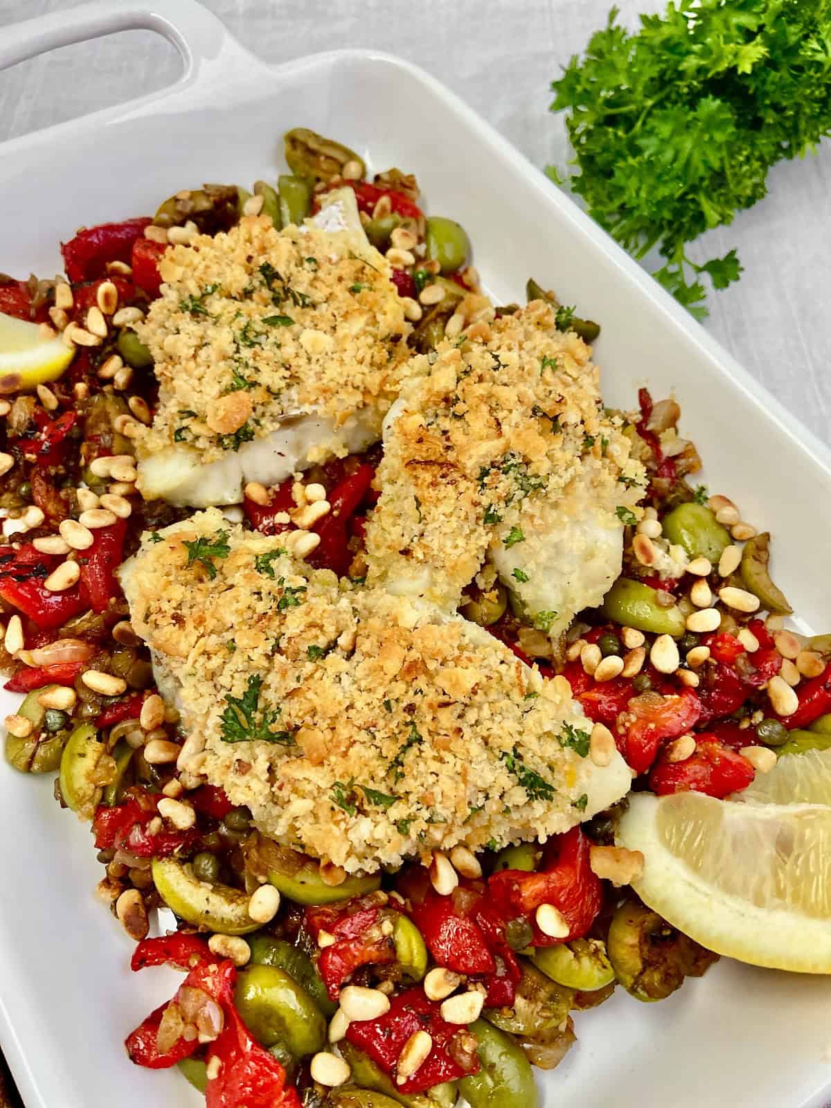 Baked cod topped with garlic breading and resting on a bed of roasted red peppers and olives.