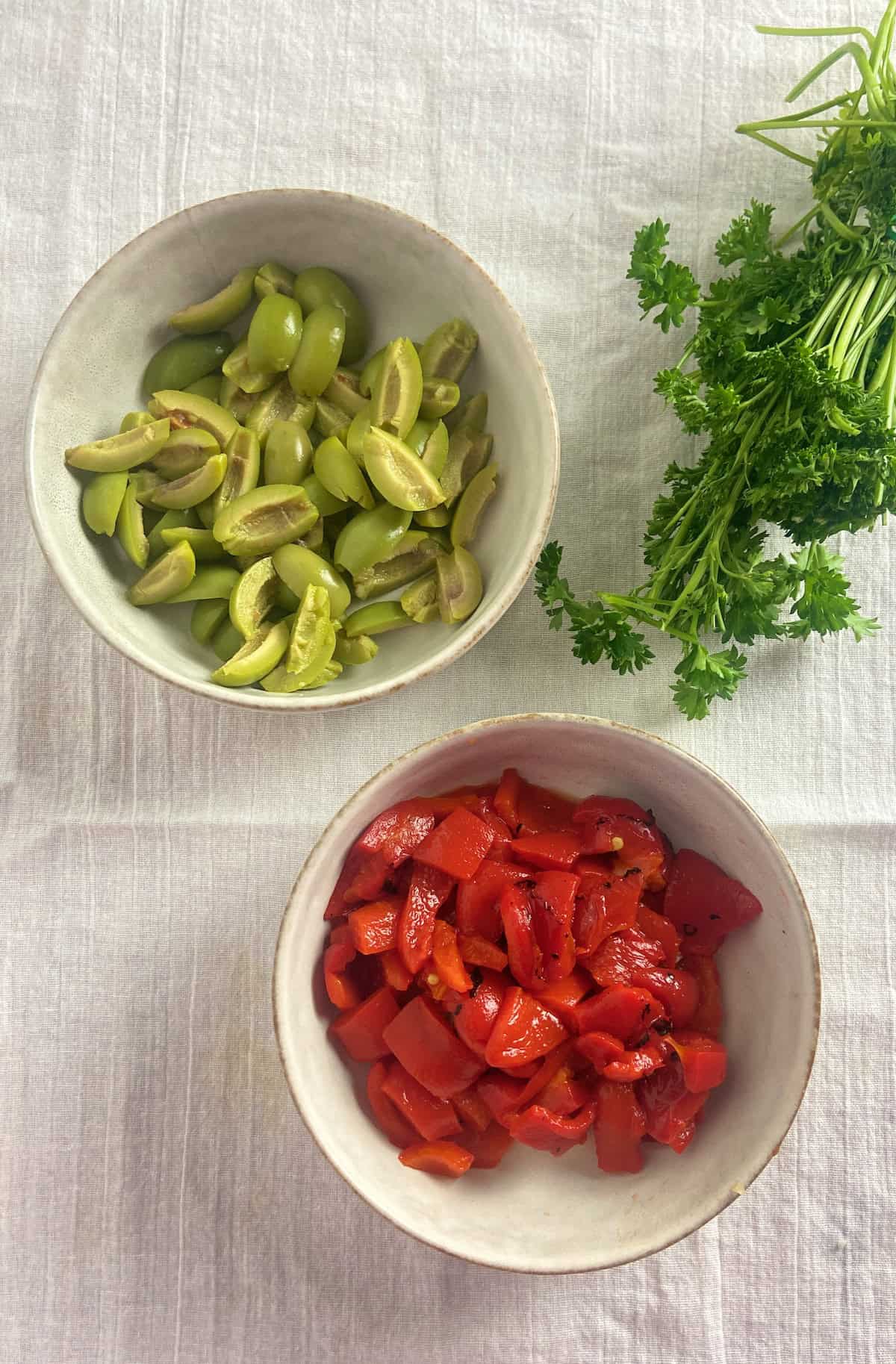 Sliced olives and diced roasted red peppers in bowls.
