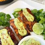 Three Tajin seasoned salmon fillets on white plate topped with avocado cream.