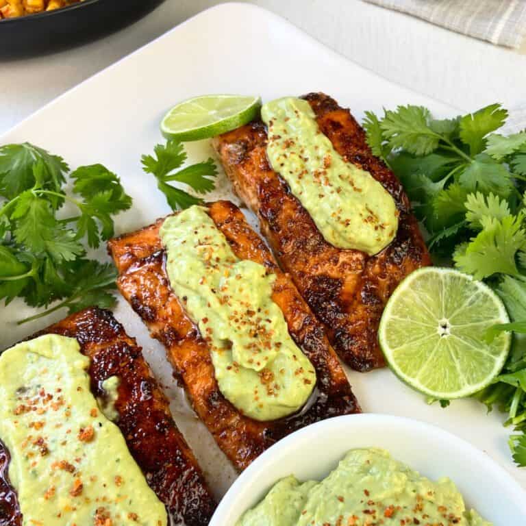 Three Tajin seasoned salmon fillets on white plate topped with avocado cream.