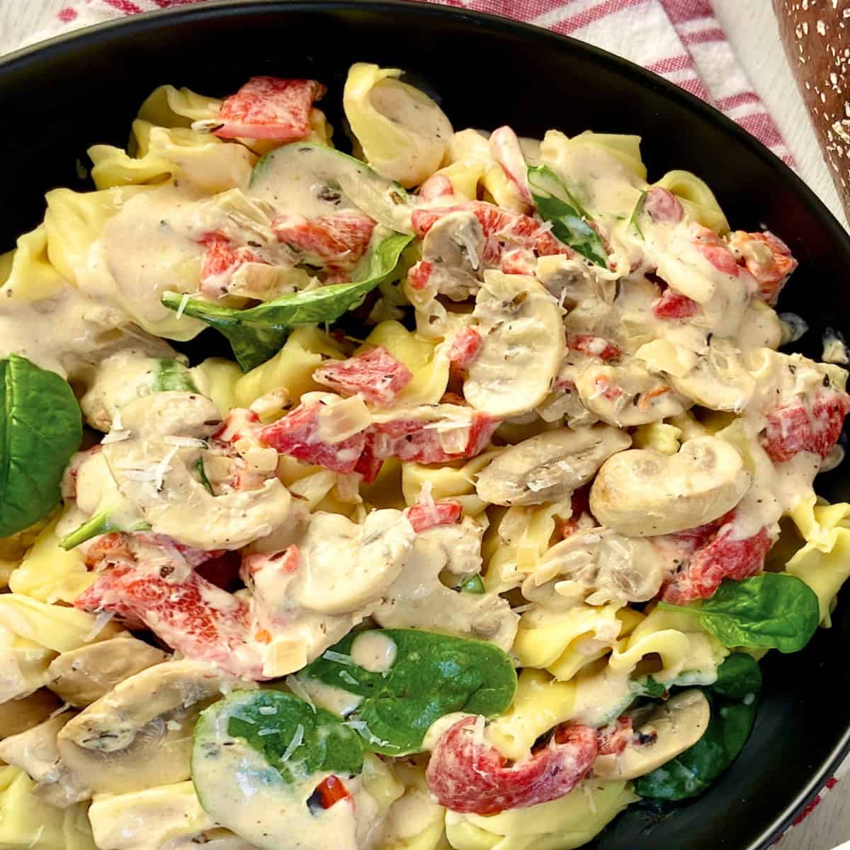 Tuscan cream sauce over tortellini in black bowl.