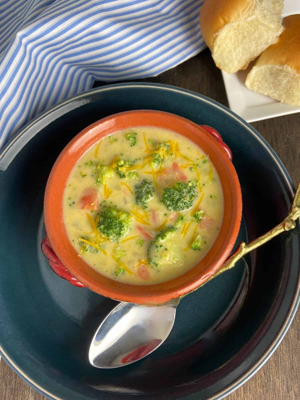 Broccoli Cheese Soup in red bowl with spoon on the side.