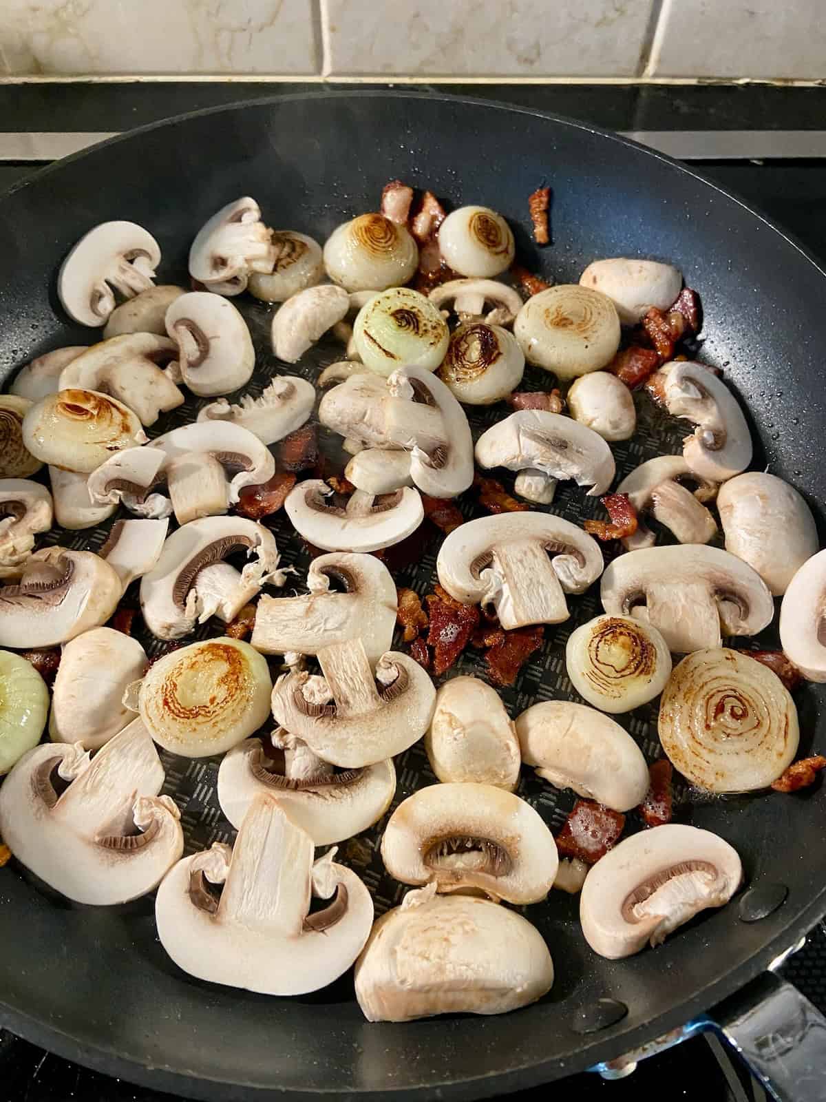 Onions, sliced mushrooms and diced bacon in skillet