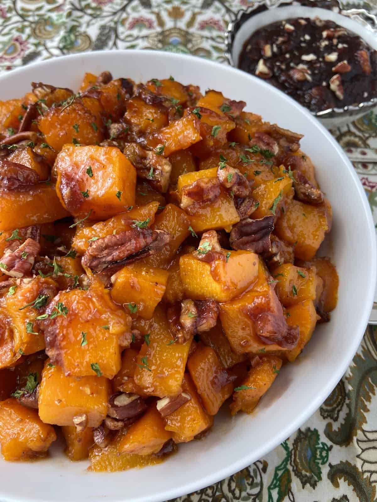 Roasted butternut squash in a white bowl garnished with chopped pecans.