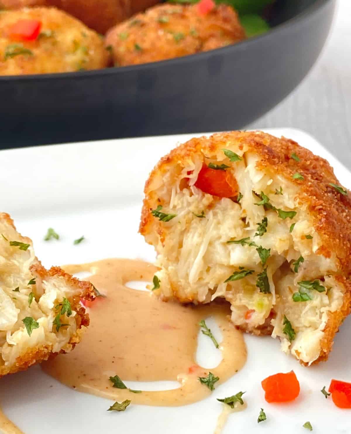 Crab ball cut in half on white plate with remoulade sauce.