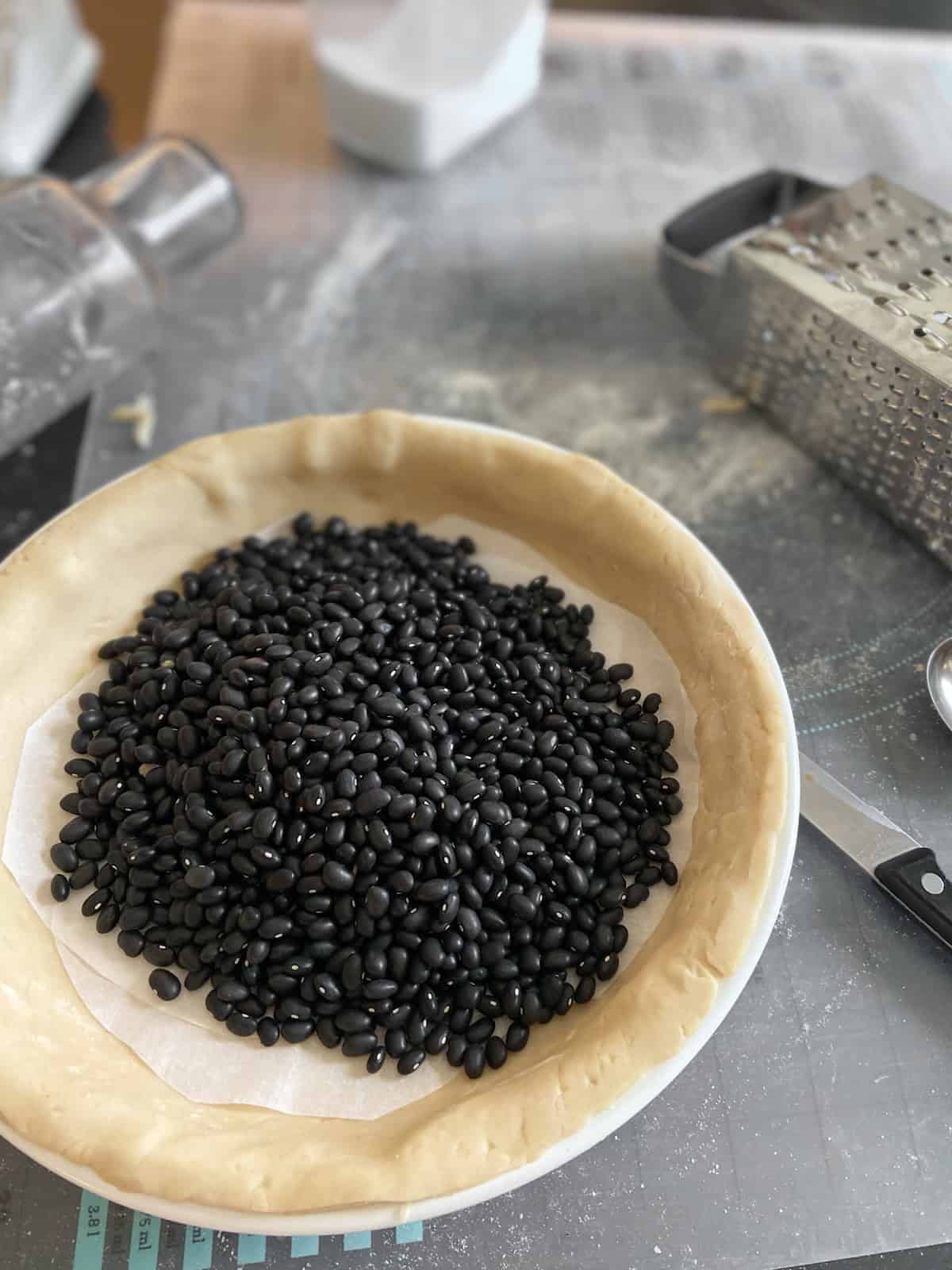 Parchment paper and dried black beans in uncooked pie shell.