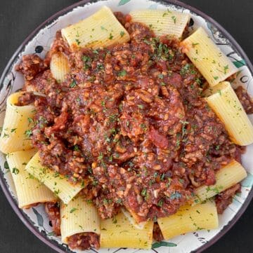 Bolognese sauce over large tubular pasta in shallow bowl.