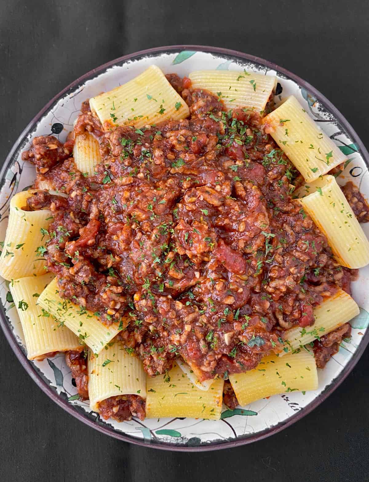 Meaty bolognese sauce served over large tubular pasta in a shallow bowl.