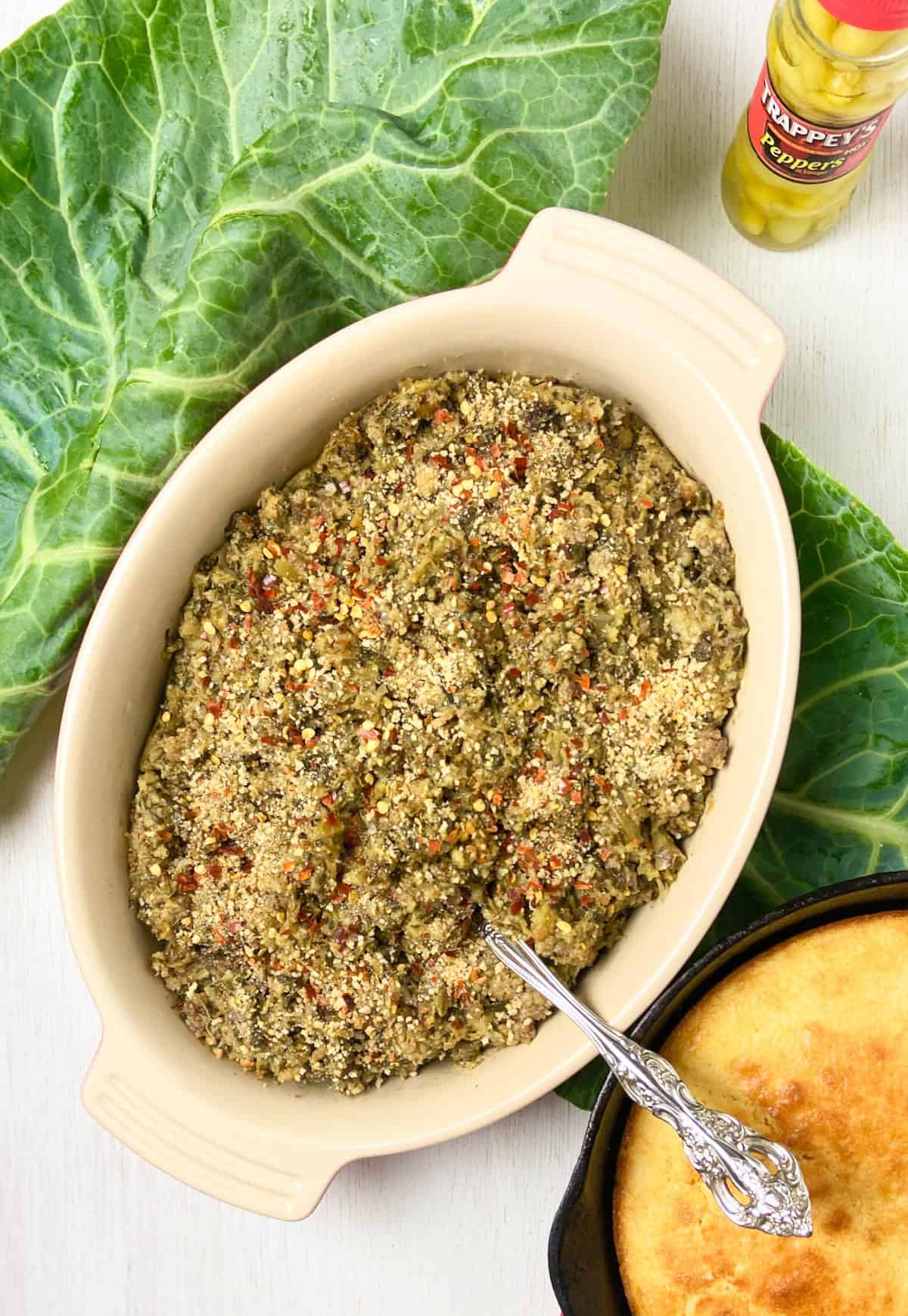 Collard green cornbread dressing in oval serving dish with a silver spoon.