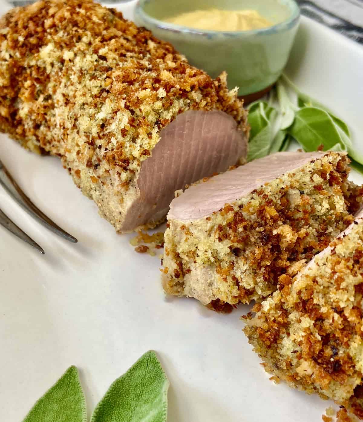 Panko crusted pork tenderloin sliced on white serving platter.