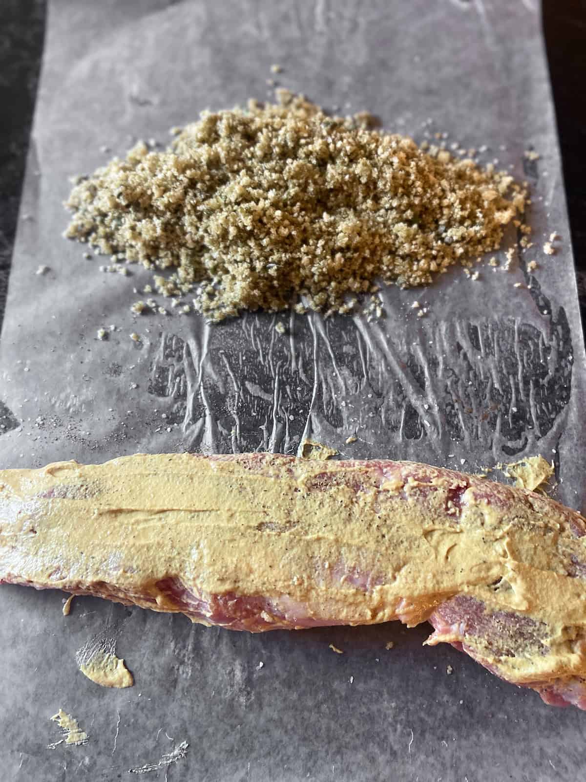Mustard coated pork tenderloin on wax paper with toasted Panko crumbs.