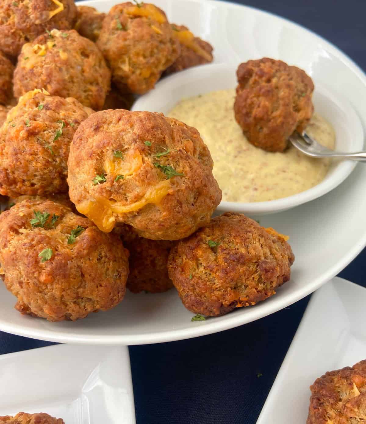 Sausage balls with mustard sauce in white serving bowl.