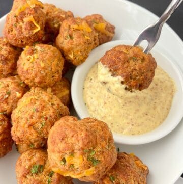Sausage ball dipped in mustard sauce on fork.