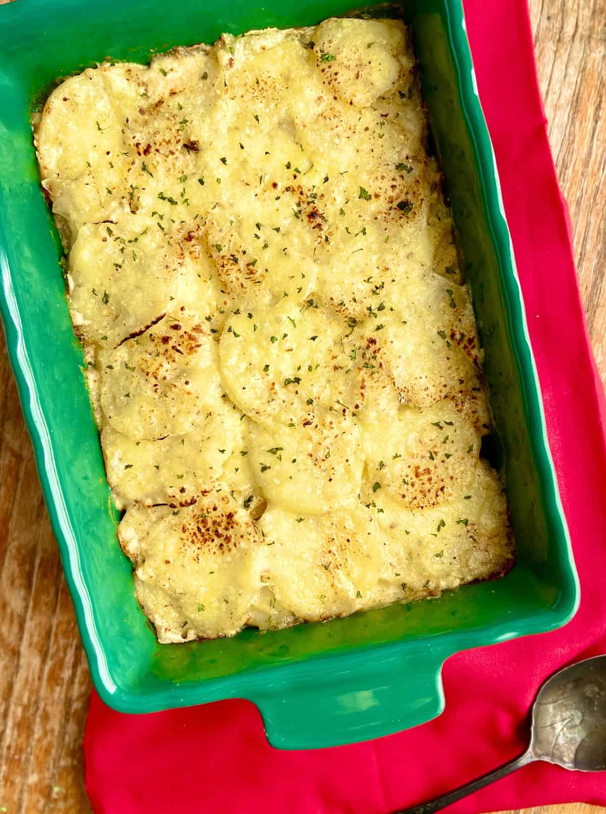 Scalloped potatoes in green dish with spoon.