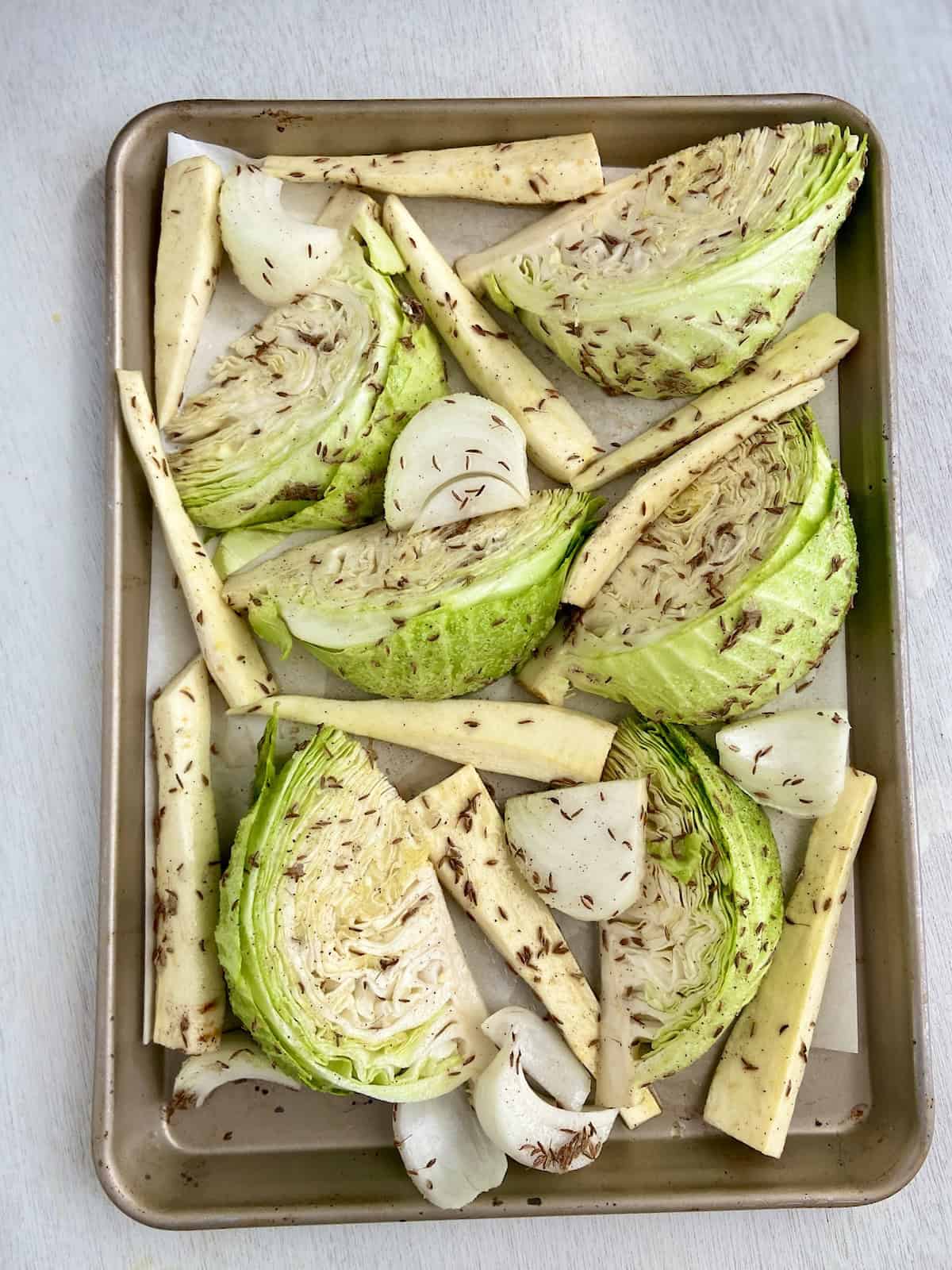 Seasoned cabbage wedges, parnips and onion on baking sheet.