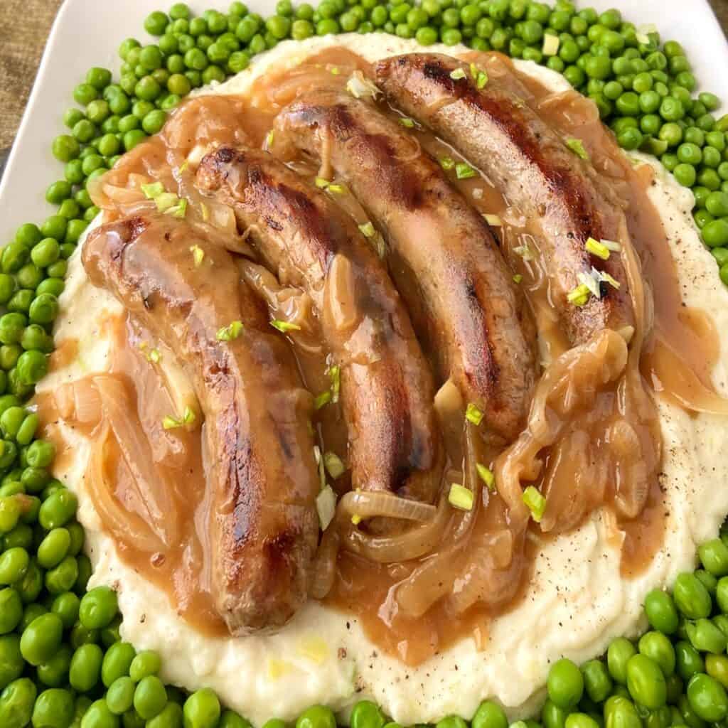 Irish bangers, mash, onion gravy and green peas on plate.