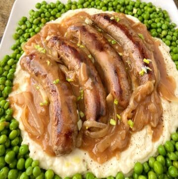 Irish bangers, mash, onion gravy and green peas on plate.