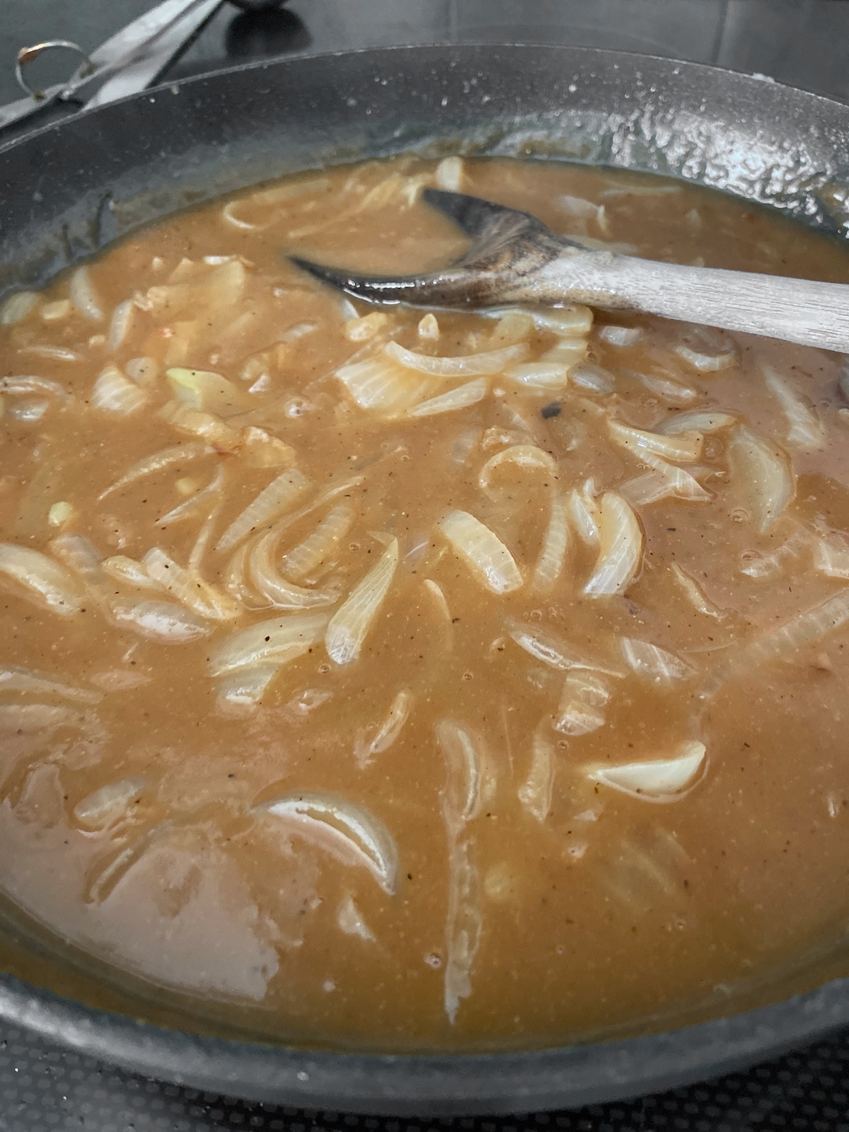 Brown onion gravy in skillet with wooden spoon.