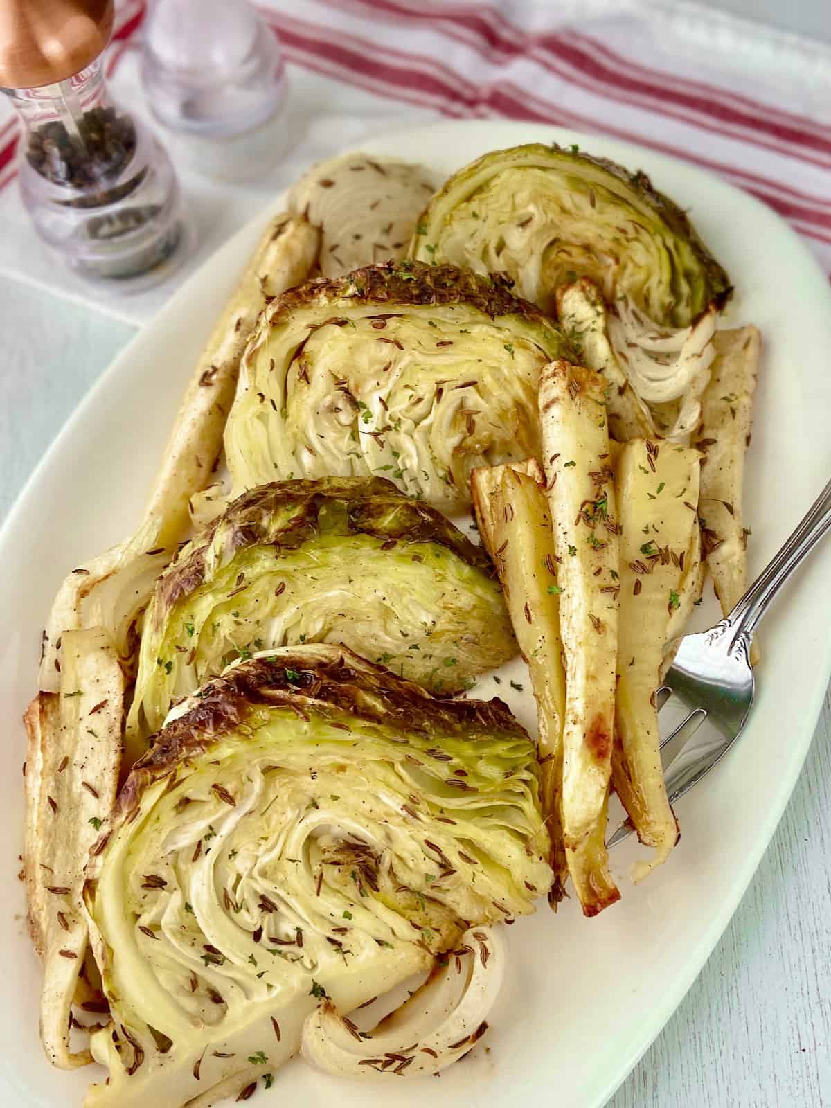 Roasted caramelized cabbage wedges and parsnips on white serving platter.