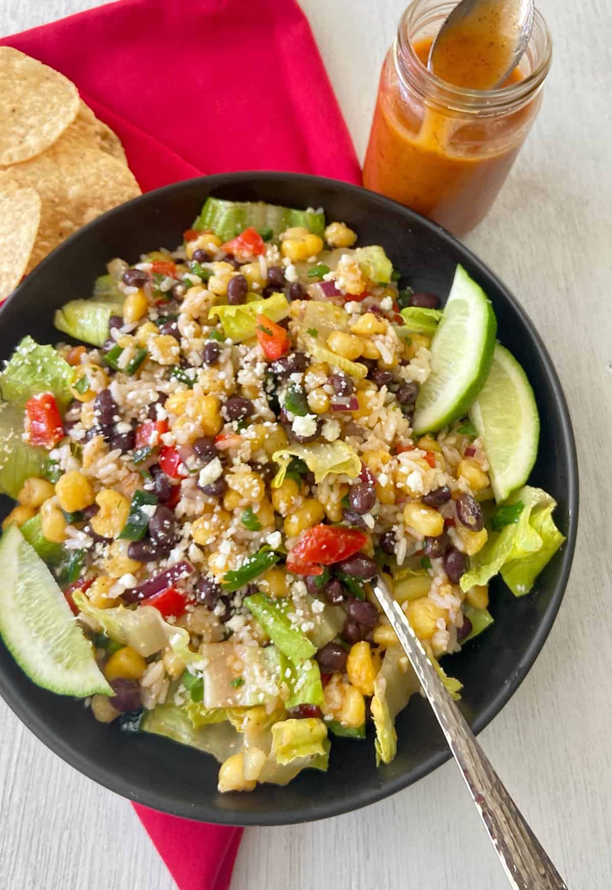 Mexican salad with hominy, black beans, red bell peppers in a black bowl.