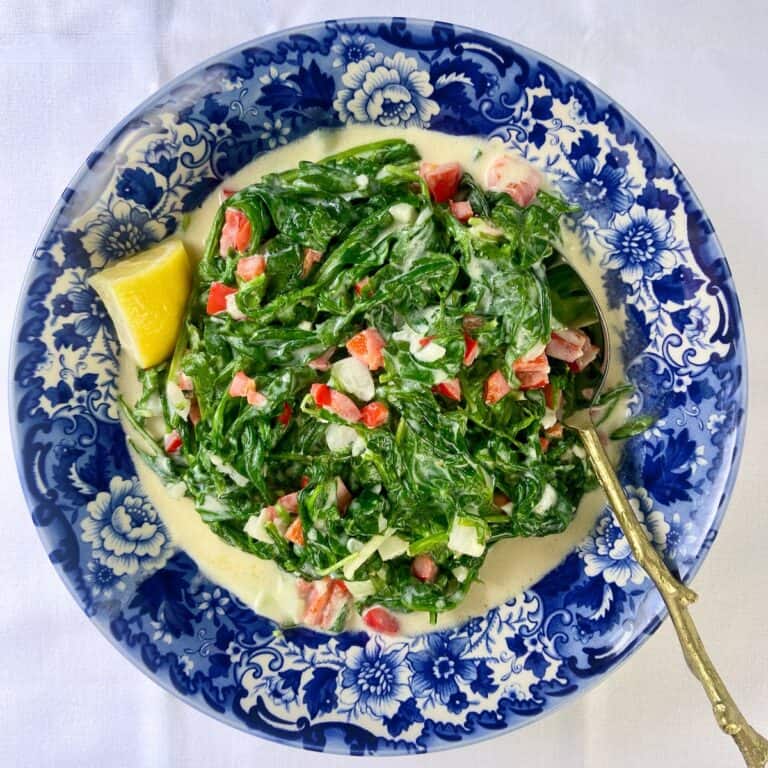 Mediterranean style creamed spinach and arugla in a decorative blue bowl.