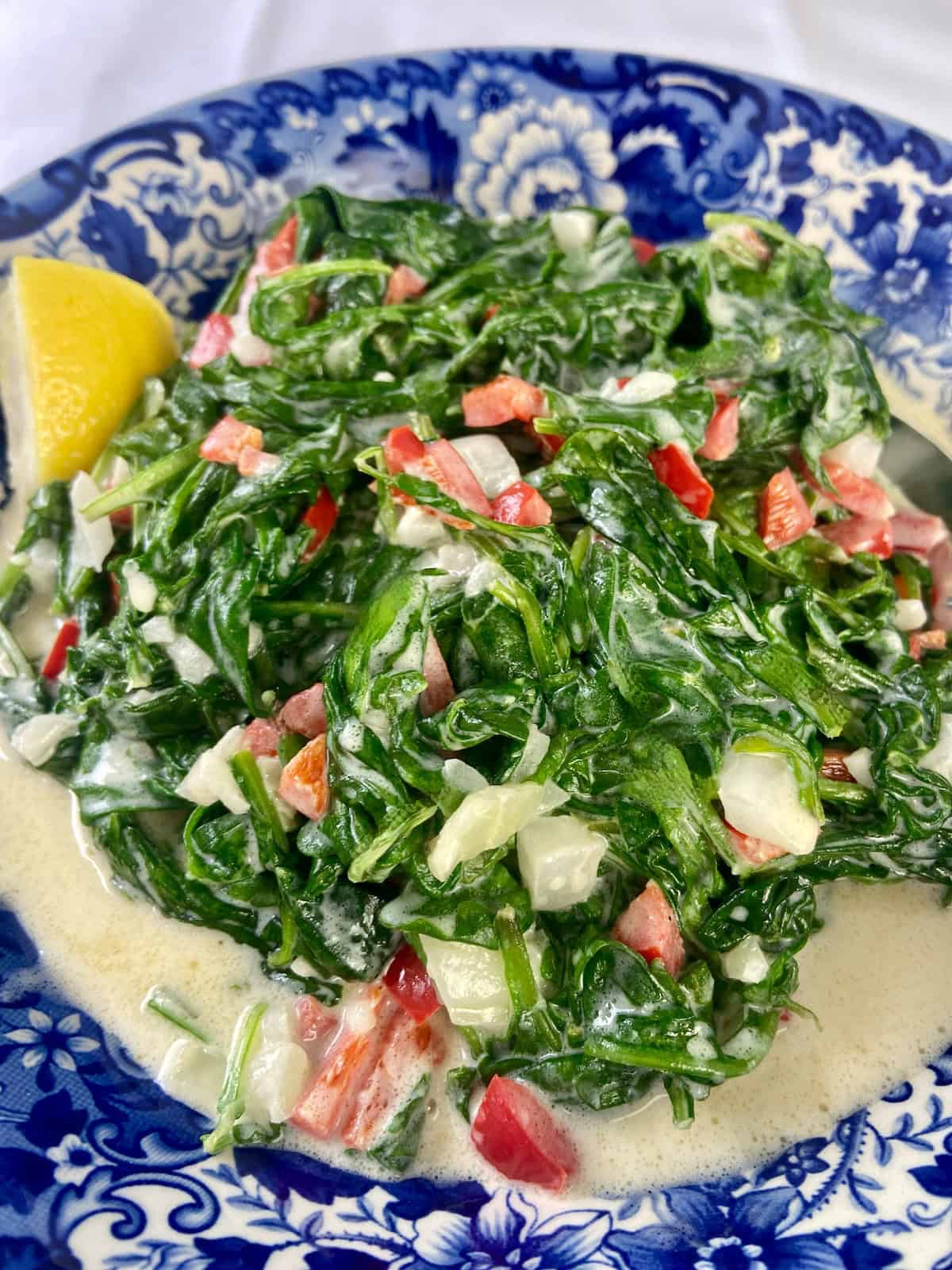 Creamed spinach in a bowl garnished with diced red bell pepper.
